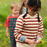 Close up of child wearing the Little Green Radicals ginger striped knitted jumper. Other children can be seen in the background. 