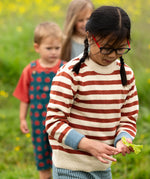 Close up of child wearing the Little Green Radicals ginger striped knitted jumper. Other children can be seen in the background. 
