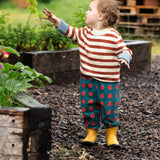 Young child wearing the Little Green Radicals ginger striped knitted jumper with repeat apple print trousers and yellow gold wellington boots.