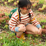 A child kneeling down wearing the Little Green Radicals ginger striped knitted jumper with blue and white pin stripe shorts and yellow gold wellington boots.