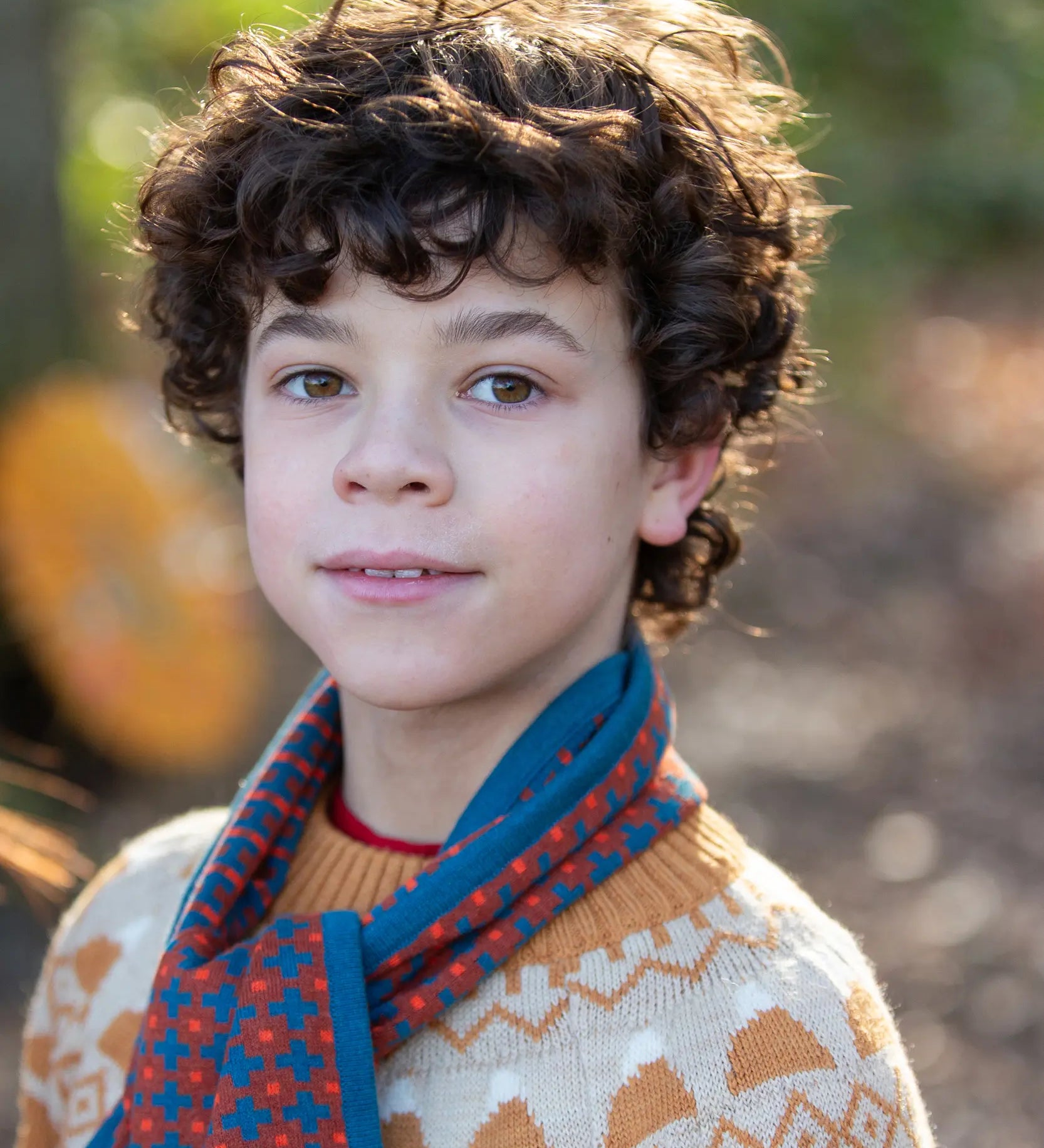 Child wearing a Little Green Radicals  ginger squares knitted scarf with a knitted jumper. 