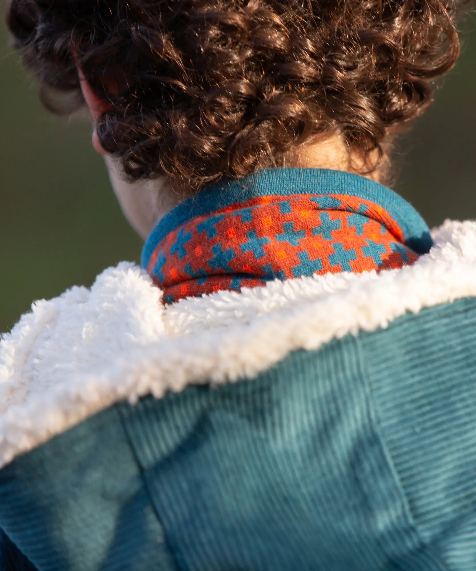 Child wearing a Little Green Radicals  ginger squares knitted scarf with a corduroy coat, view of back.