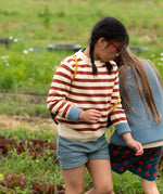 Child wearing the Little Green Radicals ginger striped knitted jumper with light blue cuffs and blue and white pin stripe shorts. 