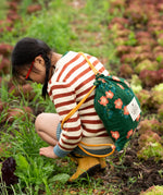 A child kneeling down wearing the Little Green Radicals ginger striped knitted jumper with blue and white pin stripe shorts and yellow gold wellington boots.