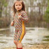 A child wearing the Little Green Radicals Vintage Flowers UPF 50+ Recycled Sunsafe Sunsuit with a pair of red wellington boots.