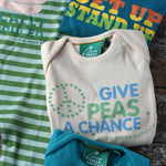 A close up of the give peas a chance slogan Little Green Radicals playsuit folded up. The other three slogan playsuits can be seen placed around it.