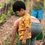 Child wearing the Little Green Radicals yellow gold summer pears short sleeve organic cotton t-shirt with green muslin shorts. 