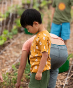 Child wearing the Little Green Radicals yellow gold summer pears short sleeve organic cotton t-shirt with green muslin shorts. 