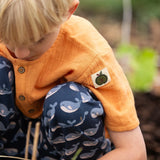 Little Green Radicals children's golden ochre yellow short sleeved henley top being worn by a child withe navy whale print joggers. .