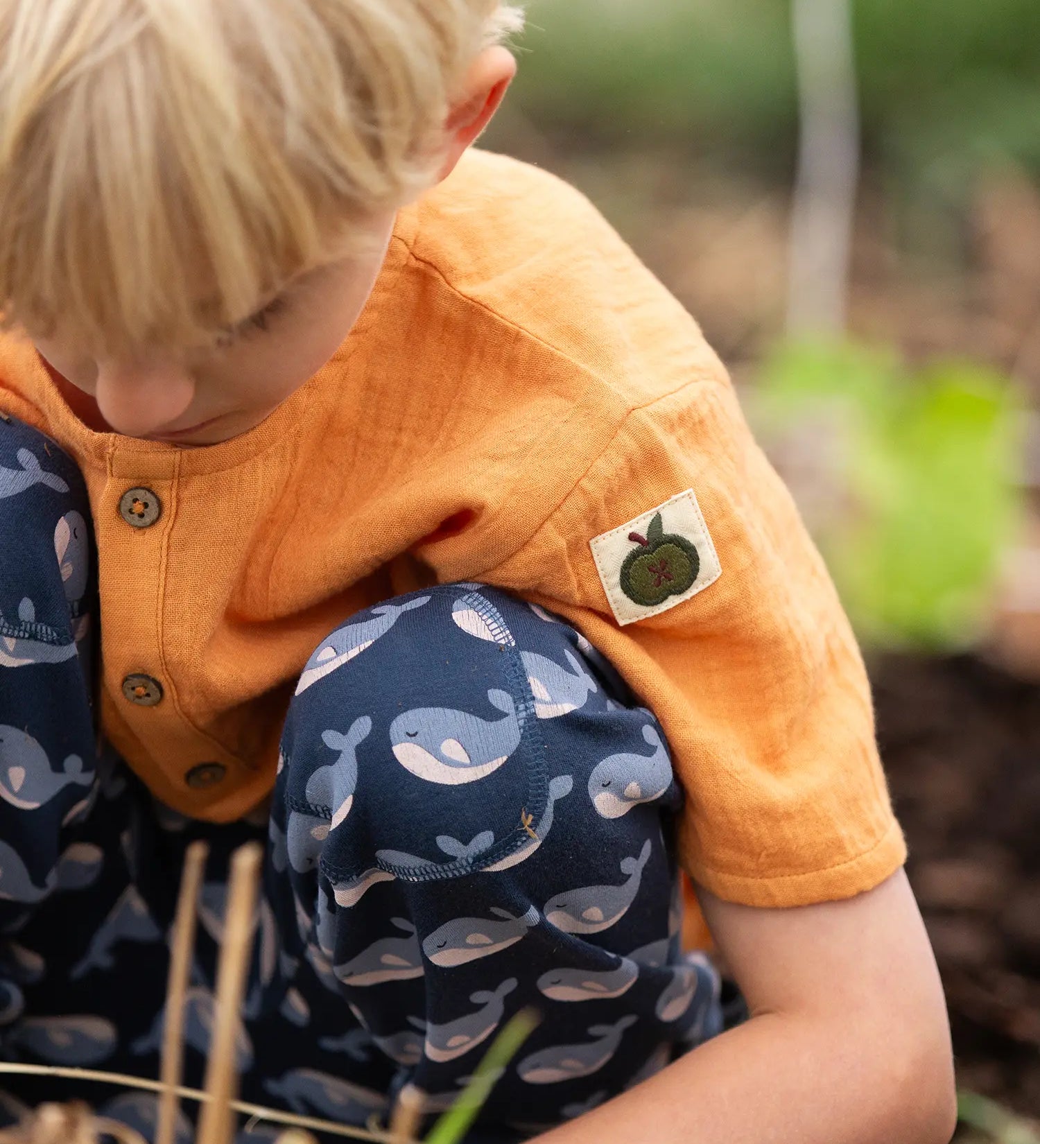 Little Green Radicals children's golden ochre yellow short sleeved henley top being worn by a child withe navy whale print joggers. .