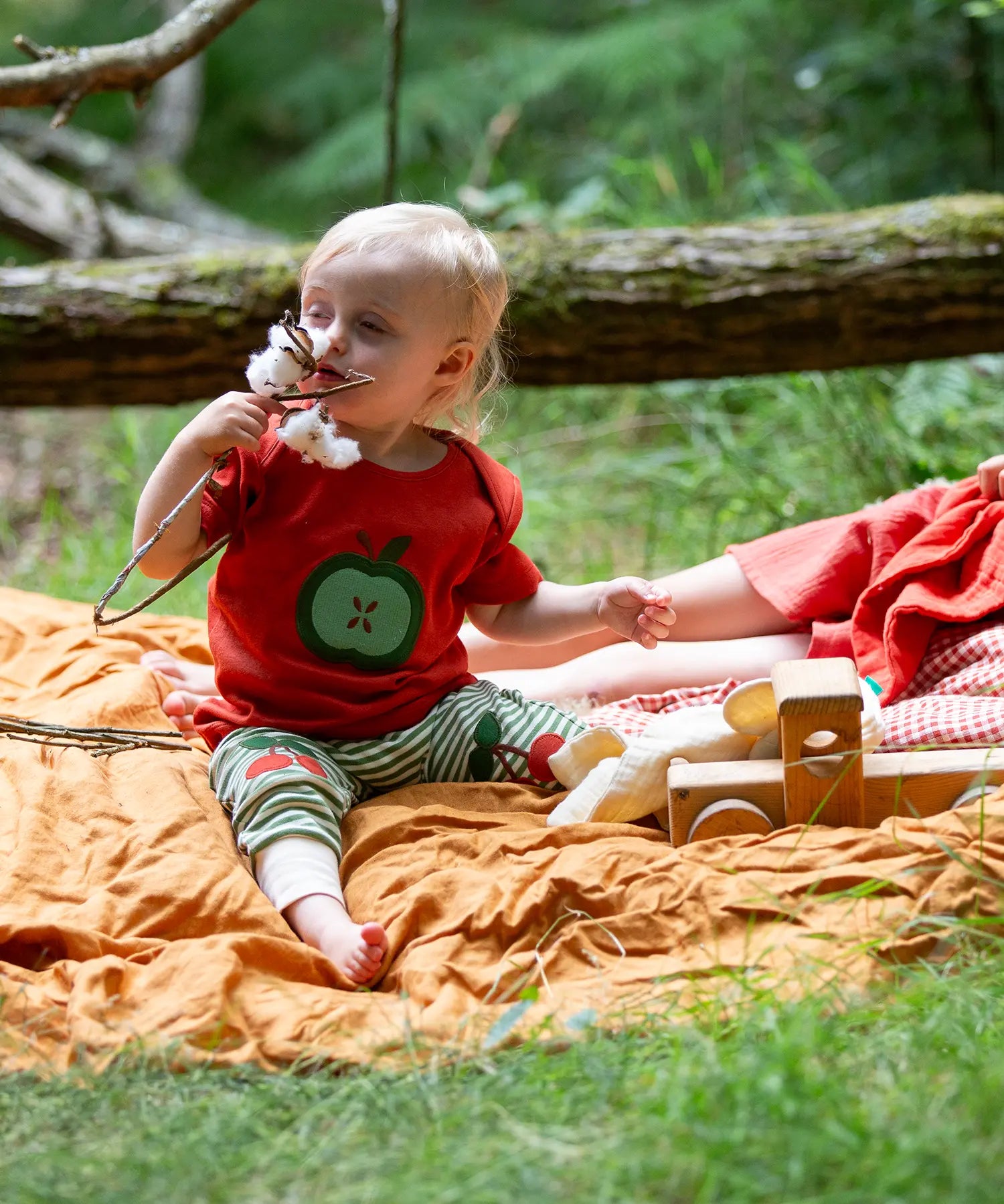 Child wearing the Little Green Radicals green apple applique organic short sleeve red t-shirt with cherry knee patch joggers.