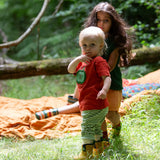 Child wearing the Little Green Radicals green apple applique organic short sleeve red t-shirt with cherry knee patch joggers and yellow wellington boots.