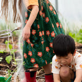Close up of the side pockets on the Little Green Radicals green orange blooms repeat print reversible pinny kids dress being worn with a yellow t-short underneath and red wellington boots.