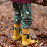 Child wearing the Little Green Radicals cosy organic cotton knee patch joggers with a woodland design print with yellow gold wellington boots.
