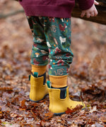 Child wearing the Little Green Radicals cosy organic cotton knee patch joggers with a woodland design print with yellow gold wellington boots.