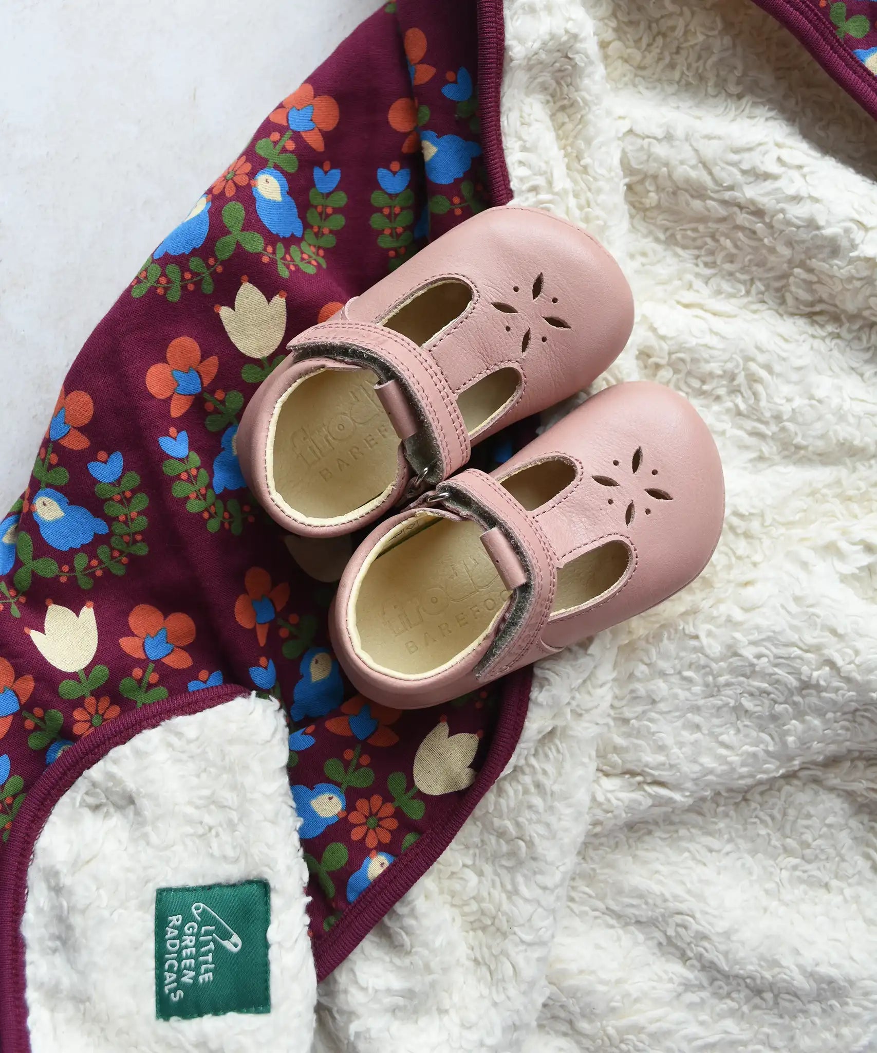 Little Green Radicals folk bird organic cotton hooded baby blanket with sherpa fleece lining with a pair of pink Froddo barefoot shoes p[laced on top.