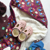 Little Green Radicals folk bird organic cotton hooded baby blanket with sherpa fleece lining with a pair of pink Froddo barefoot shoes placed on top.