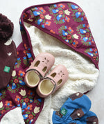 Little Green Radicals folk bird organic cotton hooded baby blanket with sherpa fleece lining with a pair of pink Froddo barefoot shoes placed on top.