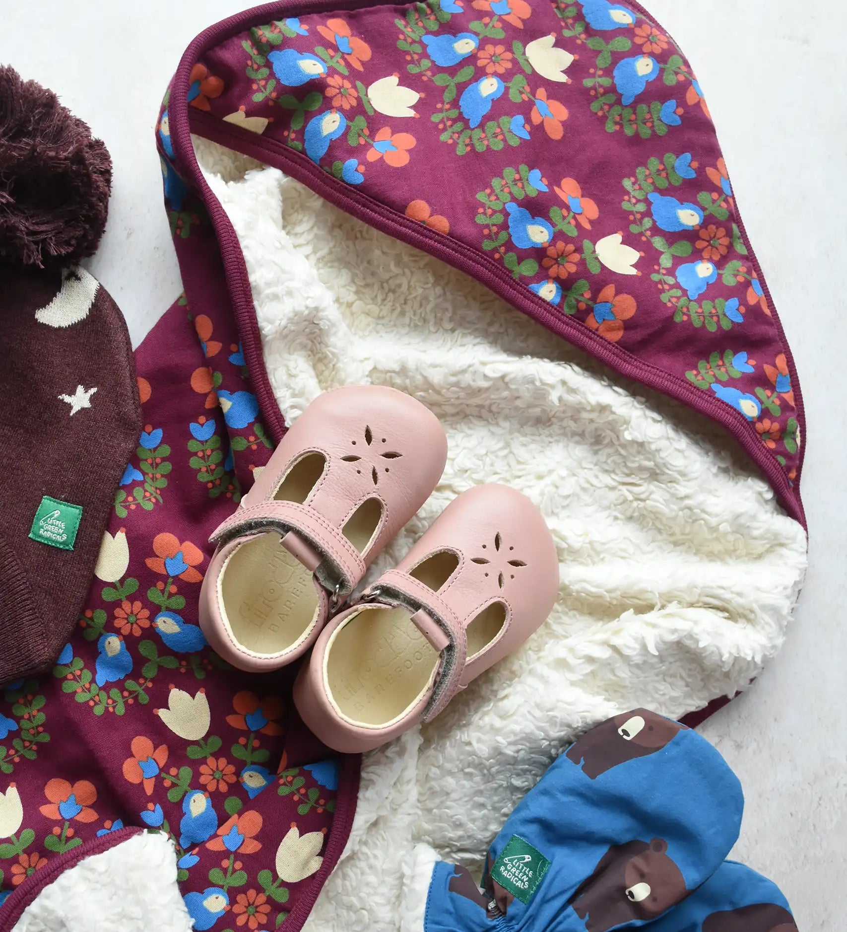 Little Green Radicals folk bird organic cotton hooded baby blanket with sherpa fleece lining with a pair of pink Froddo barefoot shoes placed on top.