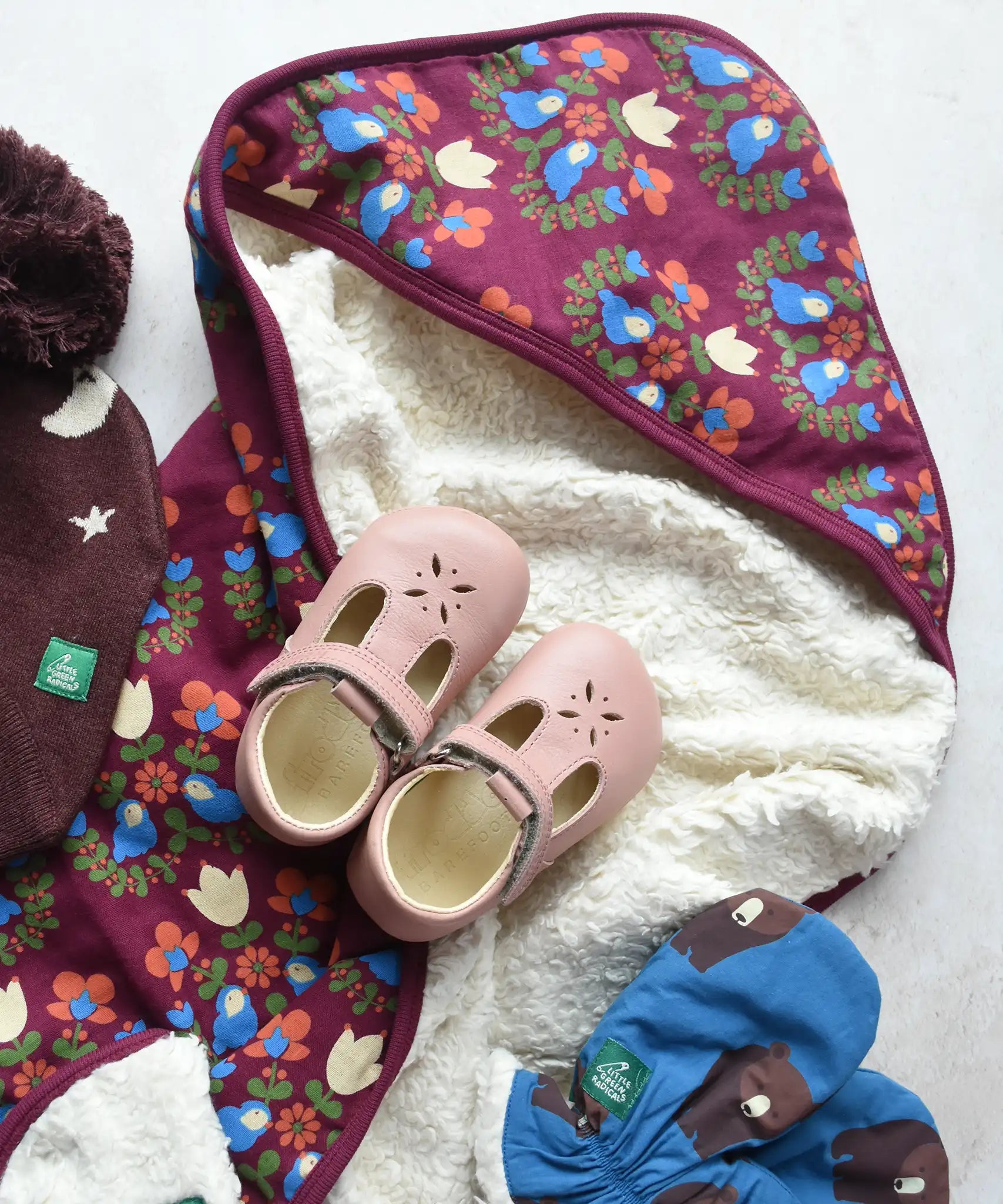 Little Green Radicals folk bird organic cotton hooded baby blanket with sherpa fleece lining with a pair of pink Froddo barefoot shoes placed on top.