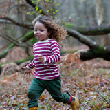 Child wearing the Little Green Radicals berry purple striped long sleeve top with green joggers and yellow gold wellington boots.