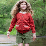 A child wearing a Little Green Radicals From One To Another Burnt Ochre Pointelle Knitted Cardigan with green coloured shorts. Little green Radicals have a wide range of organic cotton, Fairtrade children's clothing and outerwear available here at Babipur.