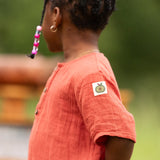 Close up of the green apple print tag on the side of the arm on the Little Green Radicals children's burnt ochre red short sleeved henley top.