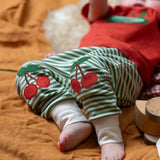 Close up of the red cherry knee appliques on the Little Green Radicals cherry knee patch green cream striped organic cotton joggers being worn.