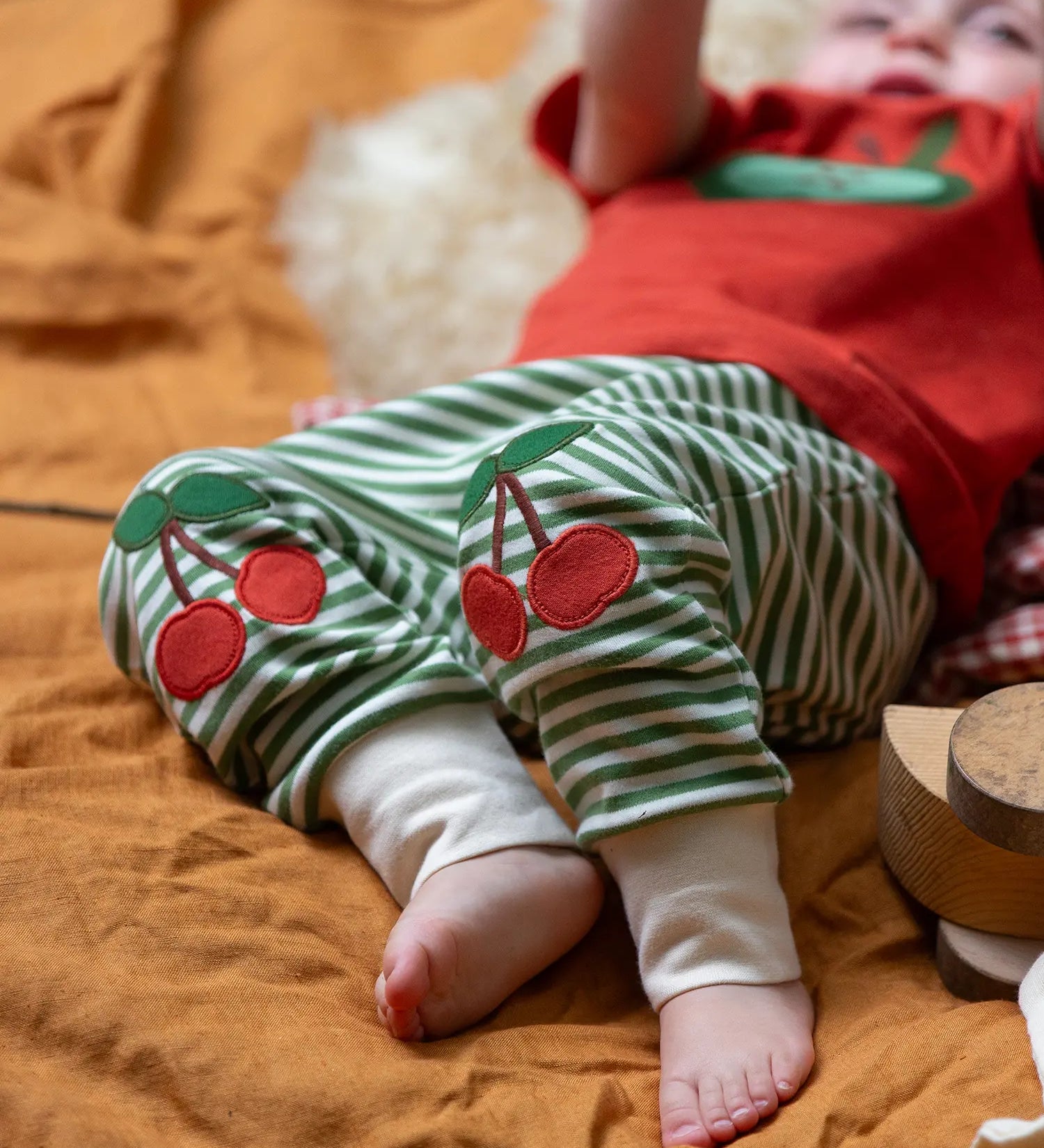 Close up of the red cherry knee appliques on the Little Green Radicals cherry knee patch green cream striped organic cotton joggers being worn.