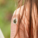 Close up of the apple tag on the arm of the Little Green Radicals kids light coral pink short sleeved henley top being worn by a child.