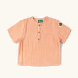 Little Green Radicals kids light coral pink short sleeved henley top with apple patch label on the side of one arms and a button up front.