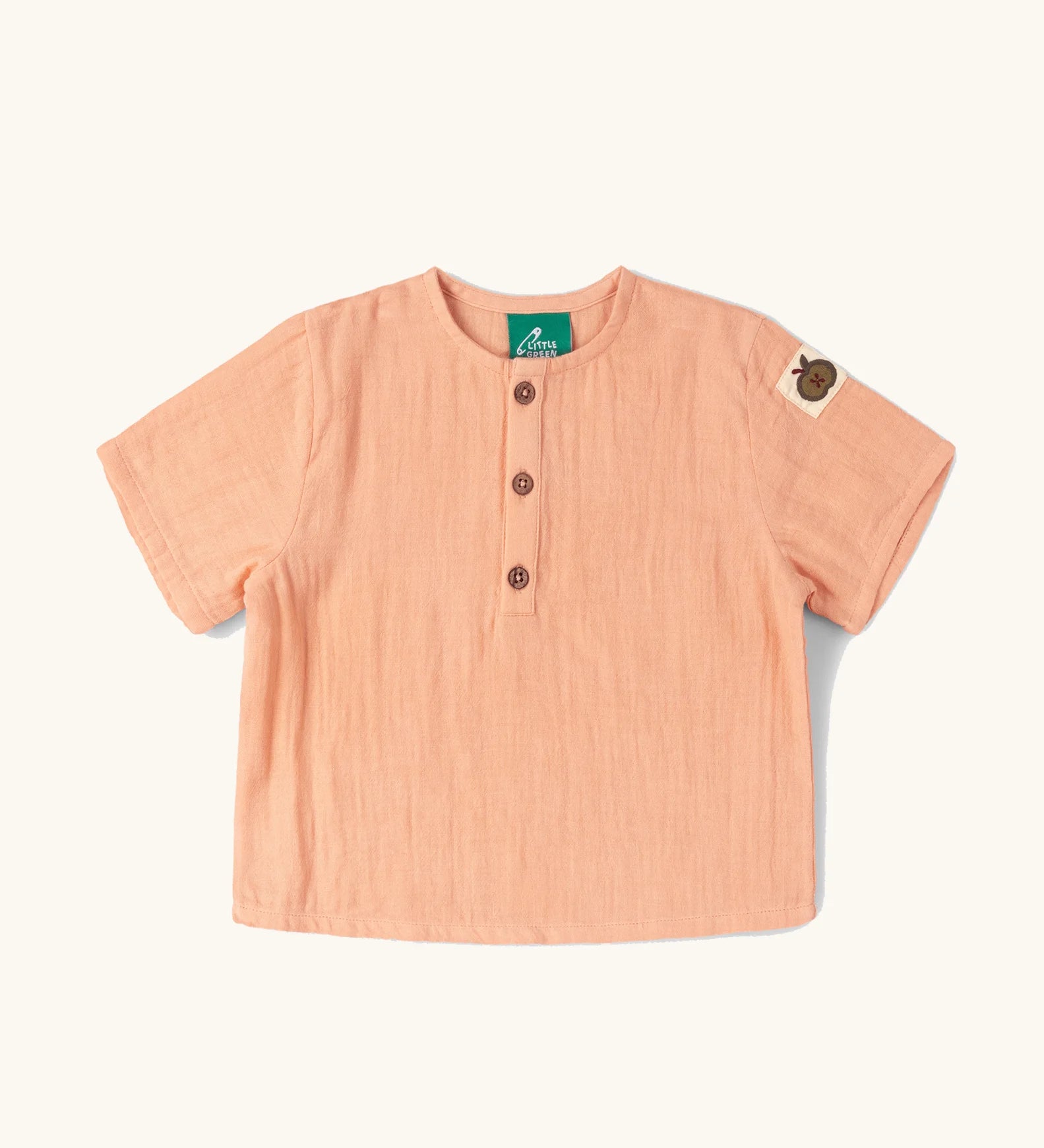 Little Green Radicals kids light coral pink short sleeved henley top with apple patch label on the side of one arms and a button up front.