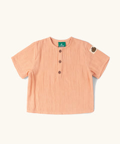 Little Green Radicals kids light coral pink short sleeved henley top with apple patch label on the side of one arms and a button up front.