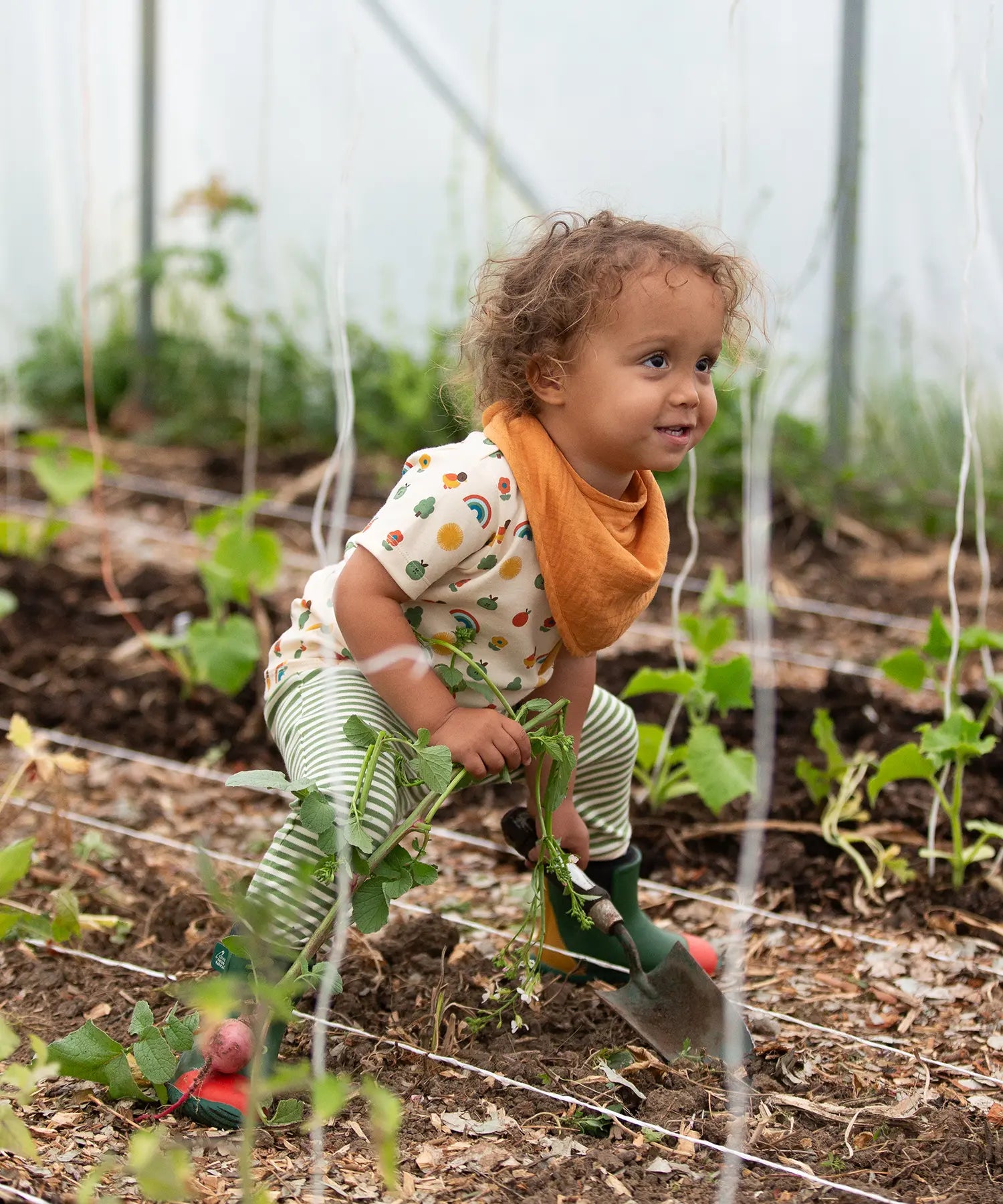 Little Green Radicals vintage style rainbows organic cotton t-shirt & jogger playset being worn. A repeat pattern top featuring nature themed illustrations with cream rainbow striped trousers.
