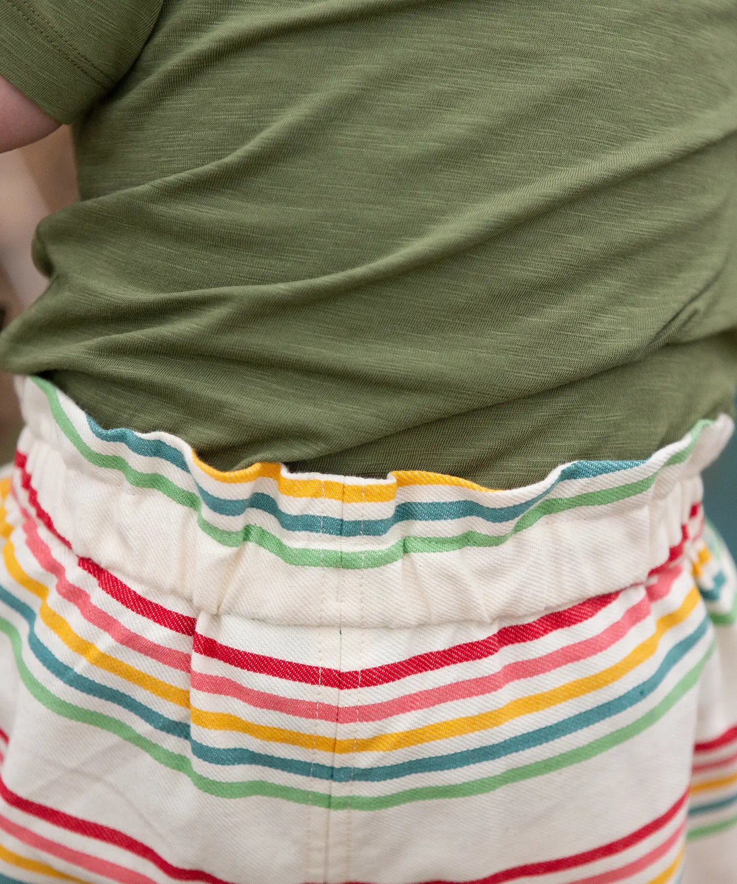 Close up of the elasticated waist on the Little Green Radicals children's cream rainbow striped by the sea twill shorts being worn. 