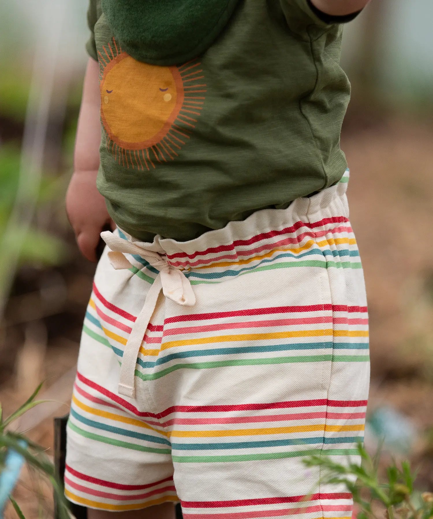 Close up of the waist tie on the Little Green Radicals children's cream rainbow striped by the sea twill shorts being worn. 