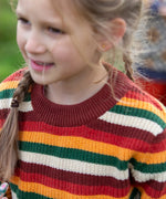 Close up of a child wearing the Little Green Radicals knitted snuggly jumper in a hazel rainbow striped design.