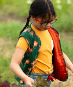 Child wearing a Little Green Radicals golden ochre yellow short sleeve essential short sleeve, organic cotton t-shirt underneath a green floral print gilet. 
 