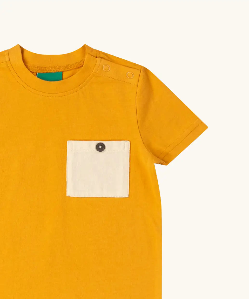 Close up of the buttoned chest pocket on the Little Green Radicals golden ochre yellow short sleeve essential short sleeve, organic cotton t-shirt. 