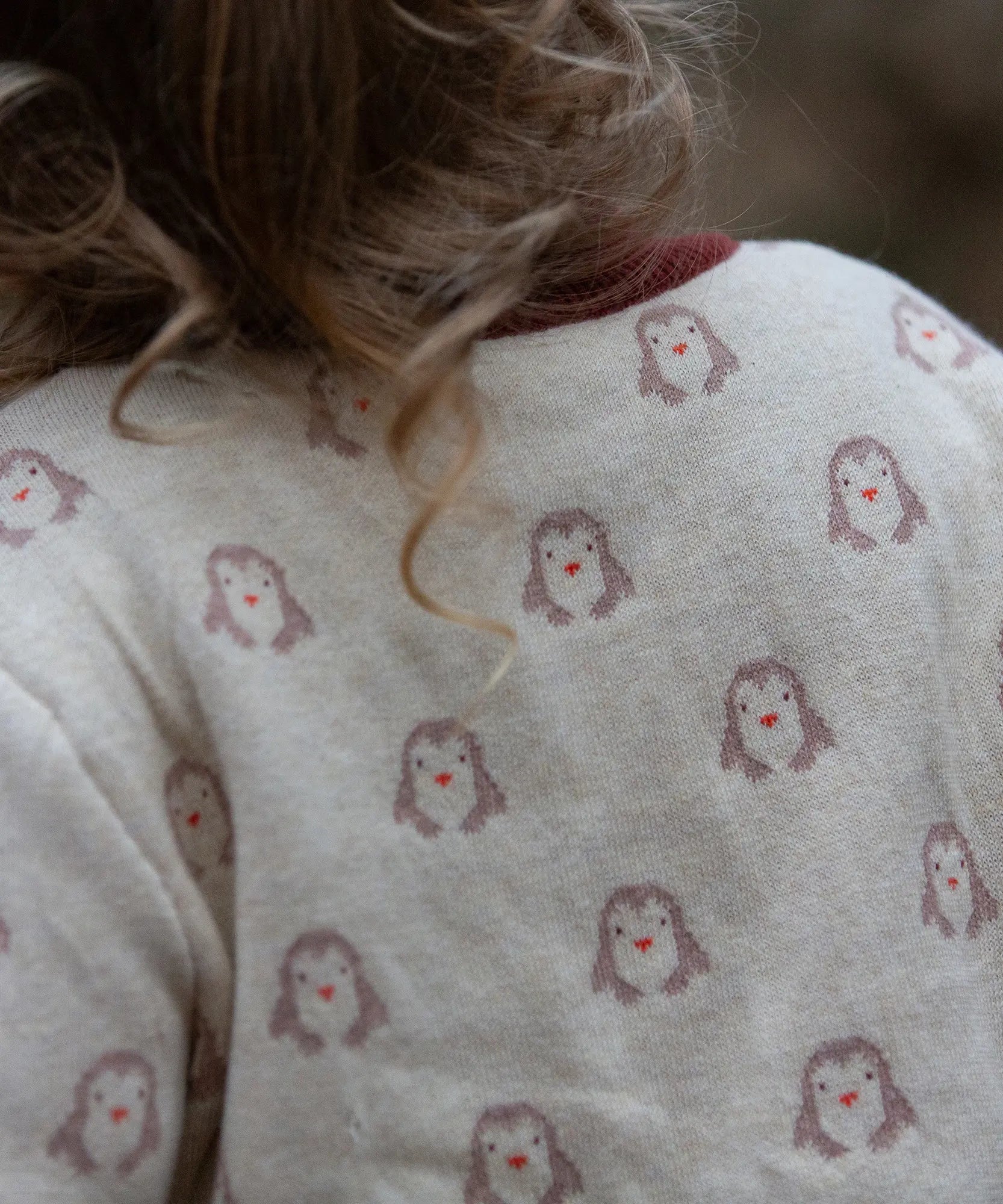 Close up of the penguin print on the Little Green Radicals organic cotton knitted cardigan with snow penguins design. Natural cream cardigan with penguins all over, maroon trim on the collar and hem line.