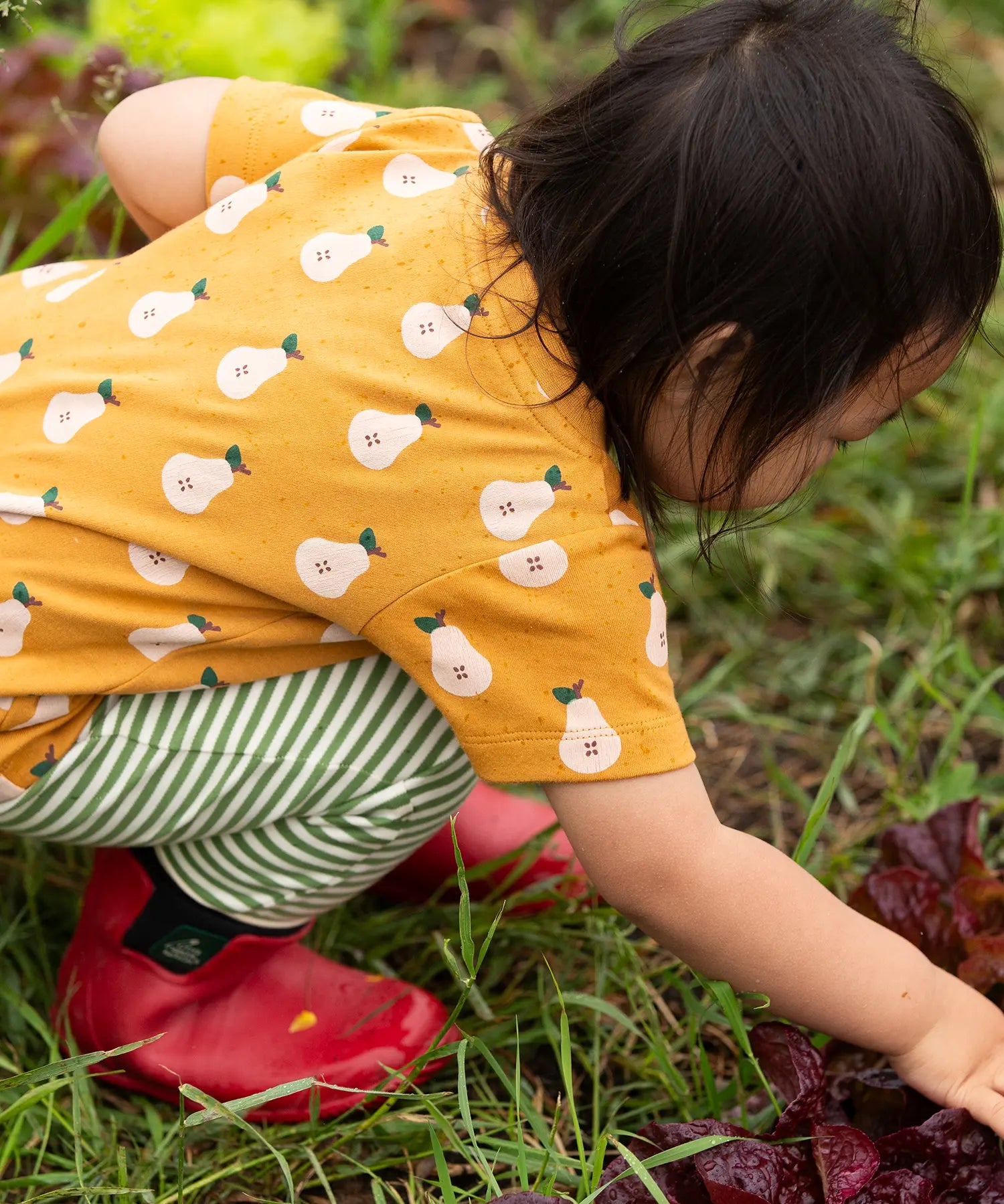 Back of the Little Green Radicals Summer pears organic cotton t-shirt and jogger playset being worn. Repeat pattern gold pear t-shirt with green and cream striped trousers.