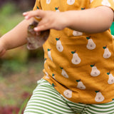 Close up of the front of the Little Green Radicals Summer pears organic cotton t-shirt and jogger playset being worn. Repeat pattern gold pear t-shirt with green and cream striped trousers.