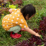 Back of the Little Green Radicals Summer pears organic cotton t-shirt and jogger playset being worn with red wellington boots. Repeat pattern gold pear t-shirt with green and cream striped trousers.