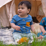 A young child sitting outdoors wearing the Little Green Radicals Kids' Organic T-shirt and Joggers Playset outfit in the  Blue Rainbows design. 