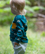 A side on view of a child wearing the Little Green Radicals Kids' Organic Top and Joggers Playset in the Turquoise Rainbows design. This play set is part of a wide range of organic cotton clothing for children available here at Babipur. 