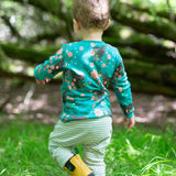 A child walking over grass, facing a way from the camera. The child is wearing the Little Green Radicals Kids' Organic Top and Joggers Playset in a Winter Rabbits design print. Little green Radicals have a wide range of organic cotton, Fairtrade children's clothing an outerwear available here at Babipur.