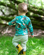 A child walking over grass, facing a way from the camera. The child is wearing the Little Green Radicals Kids' Organic Top and Joggers Playset in a Winter Rabbits design print. Little green Radicals have a wide range of organic cotton, Fairtrade children's clothing an outerwear available here at Babipur.