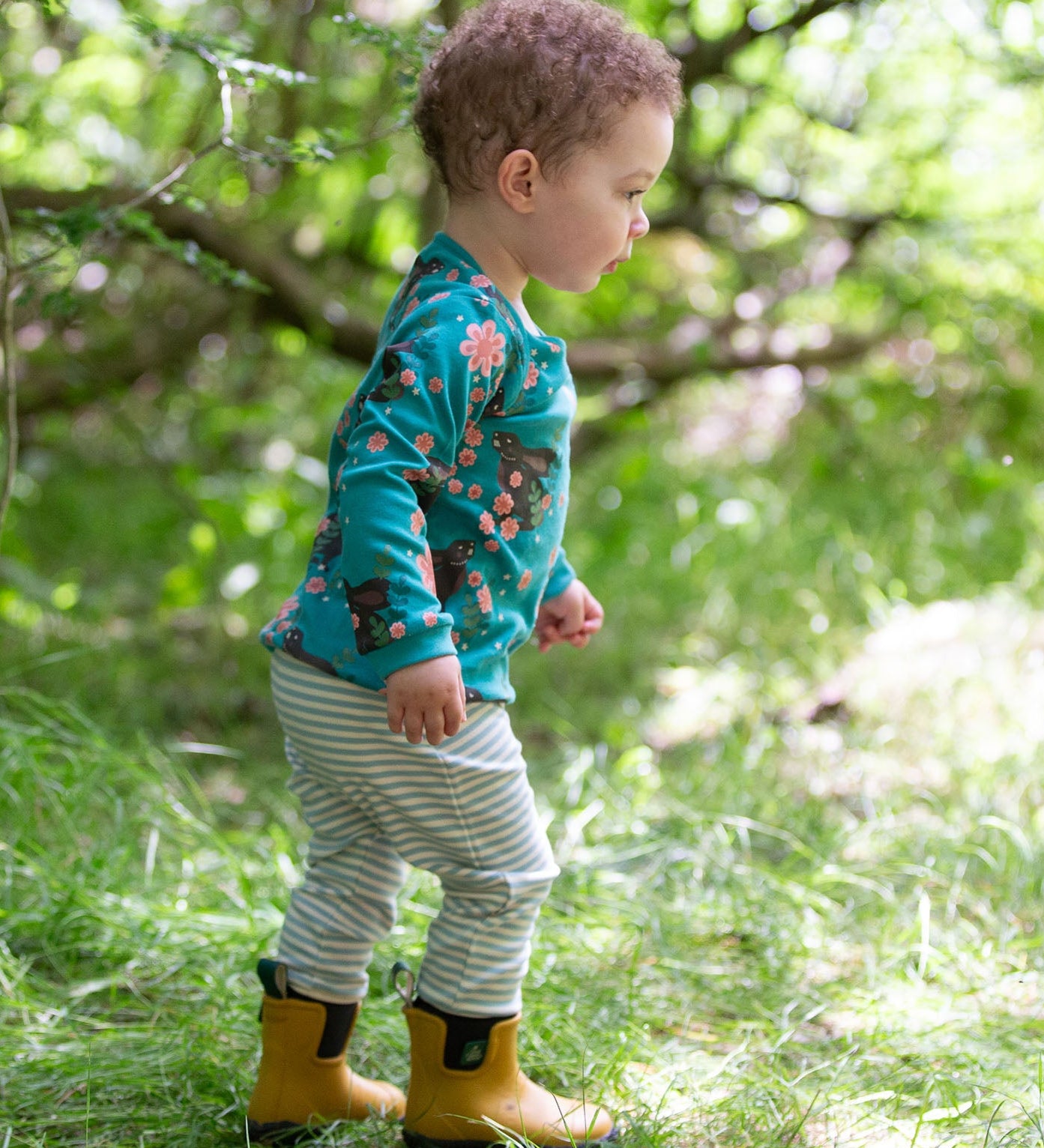 A child walking over grass wearing the Little Green Radicals Kids' Organic Top and Joggers Playset in a Winter Rabbits design print. Little green Radicals have a wide range of organic cotton, Fairtrade children's clothing an outerwear available here at Babipur.