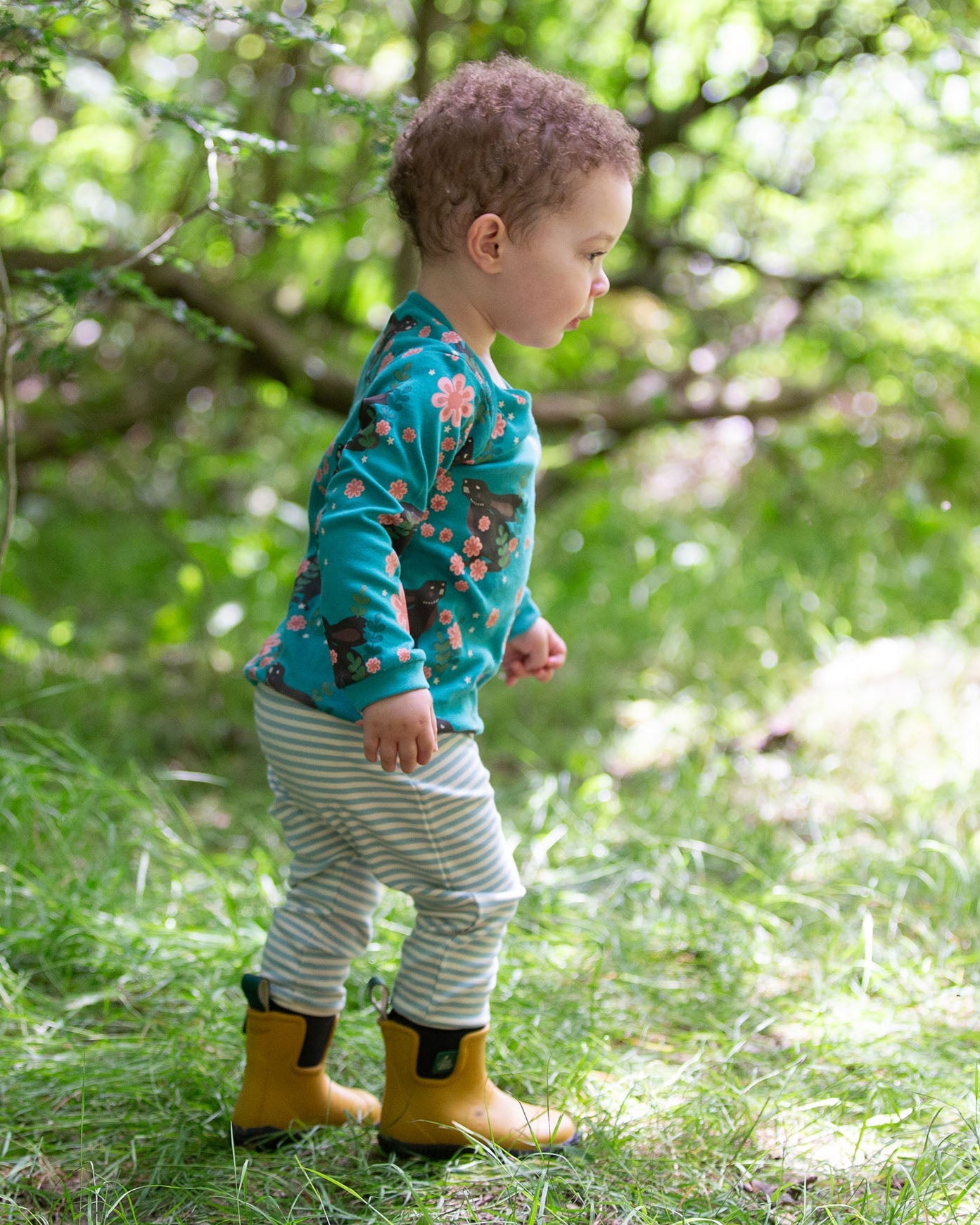 A child walking over grass wearing the Little Green Radicals Kids' Organic Top and Joggers Playset in a Winter Rabbits design print. Little green Radicals have a wide range of organic cotton, Fairtrade children's clothing an outerwear available here at Babipur.
