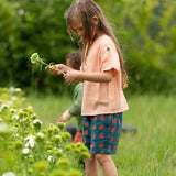 Little Green Radicals dark green blue kids organic cotton shorts with repeat apple print all worn by a child with a light orange t-shirt. 